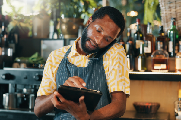 Shopkeeper Makes A Call While On Tablet 600X400